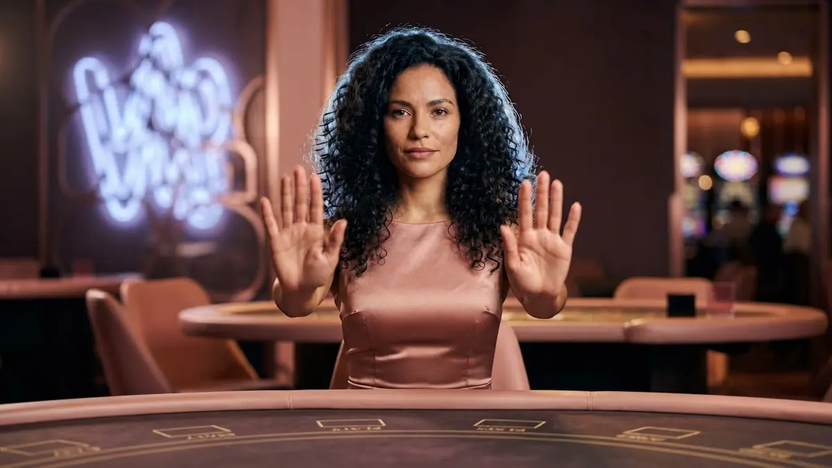 A croupier making a 'stop' gesture with her palm, behind her a blurred neon sign with no readable text